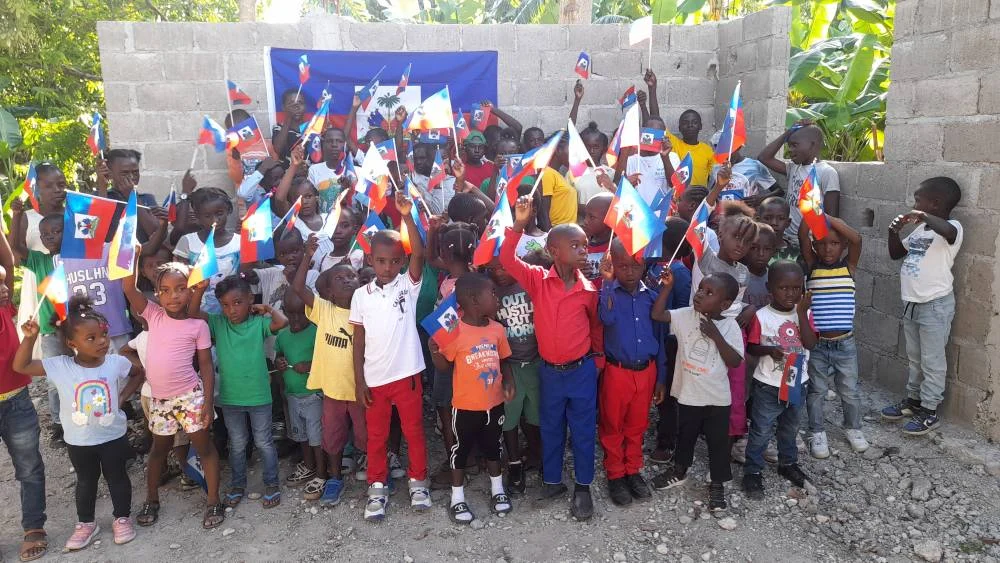Kinder bejubeln mit Fähnchen den Neubau der Kindertagesstätte in Les Cayes