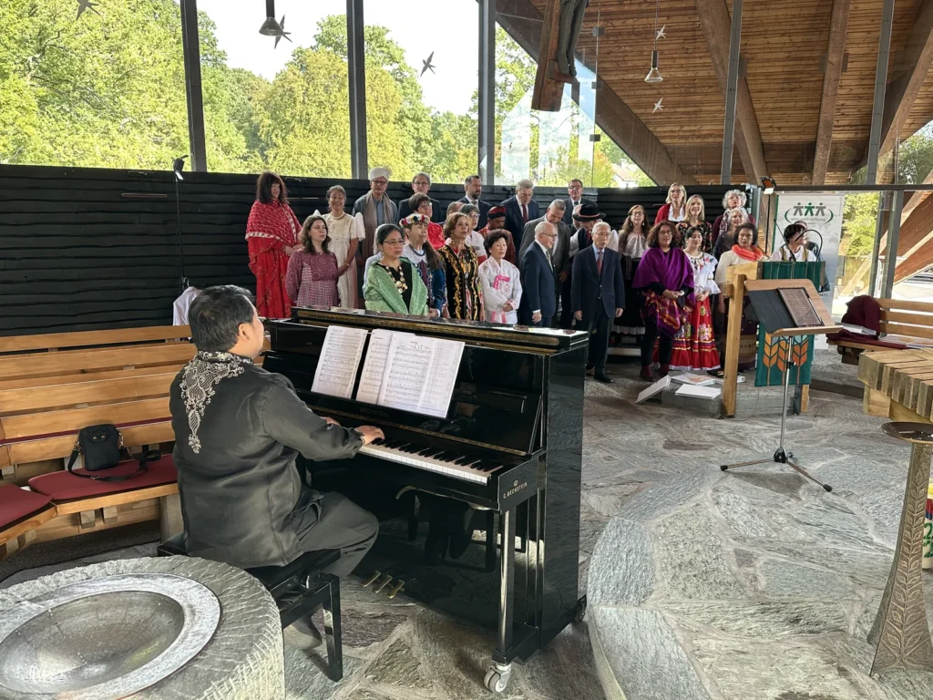 Singers in traditional costumes from all over the world at the rehearsal in the tent church, with the choir leader at the piano in the front row